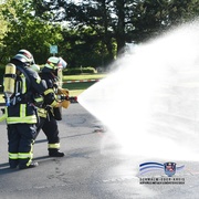 Auf dem Bild sind zwei Feuerwehrleute zu sehen. Sie haben einen Feuerwehrschlau in der Hand, aus dem Wasser kommt. in einer Ecke ist das Logo und der Schriftzug des Schwalm-Eder-Kreises zu sehen.