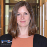 Das Bild zeigt Marina Saurwein, die Kulturbeauftragte des Schwalm-Eder-Kreises. Sie steht in einem Flur mit unscharfem Hintergrund und blickt lächelnd in die Kamera. Marina Saurwein trägt ein rostrotes Oberteil und ein schwarzes Jackett. Unten links im Bild befindet sich das Logo des Schwalm-Eder-Kreises mit dem Schriftzug „Der Kreis mit den schönsten Ecken“.