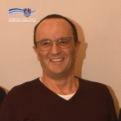 Porträt von Volker Fey. Er lächelt in die Kamera und trägt eine Brille sowie einen dunklen Pullover. Oben links im Bild ist das Logo des Schwalm-Eder-Kreises zu sehen.