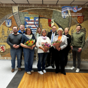 Mehrere Erwachsene stehen in zwei Reihen in einem Innenraum vor einer großen Wandgestaltung mit Wappen und dem Schriftzug „Schwalm-Eder-Kreis“. Drei Frauen in der vorderen Reihe halten Blumensträuße in den Händen. Die Gruppe blickt in die Kamera und wirkt freundlich und feierlich. Oben rechts ist das Logo des Schwalm-Eder-Kreises mit dem Schriftzug „Der Kreis mit den schönsten Ecken“ eingeblendet.