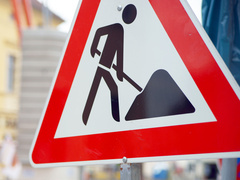 Nahaufnahme eines rot-weißen Baustellenschilds mit dem Symbol eines Arbeiters, der mit einer Schaufel Erde bewegt. Im Hintergrund sind unscharf Absperrungen und Baustellenmaterialien zu erkennen. Unten rechts ist das Logo des Schwalm-Eder-Kreises mit dem Schriftzug „Der Kreis mit den schönsten Ecken“ eingeblendet.