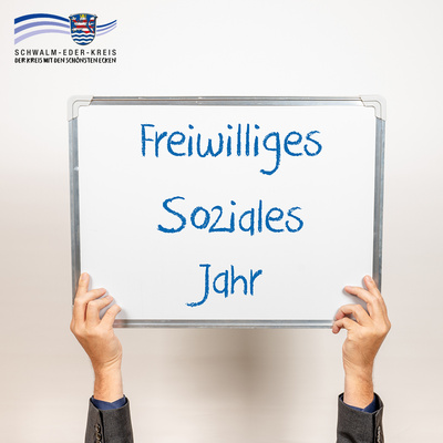 Zwei Hände halten ein Whiteboard hoch, auf dem in blauer Schrift steht: „Freiwilliges Soziales Jahr“. Der Hintergrund ist neutral beige. Oben links ist das Logo des Schwalm-Eder-Kreises mit dem Schriftzug „Der Kreis mit den schönsten Ecken“ eingeblendet.