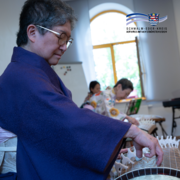 Im Vordergrund ist Frau Mizue Kishimoto-Angres am Koto, einem japanischen Instrument zu sehen.