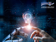 Eine menschliche Hand und eine Roboterhand berühren sich sanft mit den Fingerspitzen. Zwischen ihnen schwebt eine leuchtende Glühbirne mit einem stilisierten Gehirn im Inneren – ein Symbol für künstliche Intelligenz und Innovation. Im Hintergrund sind digitale Schaltkreise und Datenströme auf einem dunkelblauen, futuristischen Interface zu sehen. Oben rechts ist das Logo des Schwalm-Eder-Kreises eingeblendet.