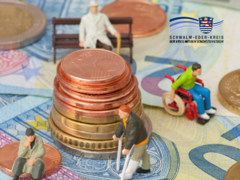 Auf dem Bild liegen verschiedene Euro-Geldscheine und Münzen, auf denen kleine Figuren platziert sind. Die Figuren stellen Menschen mit unterschiedlichen Lebenslagen dar – zum Beispiel eine Person im Rollstuhl, eine ältere Person mit Gehhilfen und eine sitzende Person. In der Bildmitte befindet sich ein gestapelter Münzturm. Oben rechts ist das Logo des Schwalm-Eder-Kreises zu sehen.