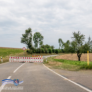Eine Landstraße ist durch eine rot-weiße Absperrung mit gelben Warnleuchten vollständig gesperrt. Dahinter verläuft die Straße leicht ansteigend durch eine offene Landschaft mit Feldern, Grasflächen und einigen Bäumen. Am linken Rand steht ein Verkehrsschild mit rotem Kreis („Einfahrt verboten“). Unten links ist das Logo des Schwalm-Eder-Kreises mit dem Schriftzug „Der Kreis mit den schönsten Ecken“