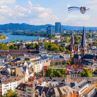 Panoramablick über die Stadt Bonn bei sonnigem Wetter. Im Vordergrund sind historische Gebäude, Kirchen mit Türmen und Baukräne zu sehen, im Hintergrund der Rhein, moderne Hochhäuser und bewaldete Hügel. Oben rechts befindet sich das Logo des Schwalm-Eder-Kreises.