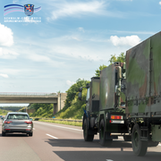 Auf dem Bild ist ein olivgrüner LKW der Bundeswehr mit Tarnlackierung zu sehen, der auf der Autobahn fährt. Neben ihm fährt ein silberner PKW. Im Hintergrund erkennt man eine Autobahnbrücke, darüber ein blauer Himmel mit wenigen Wolken. In der linken oberen Ecke ist das Logo des Schwalm-Eder-Kreises mit dem Schriftzug „Schwalm-Eder-Kreis – Der Kreis mit den schönsten Ecken“ eingefügt.