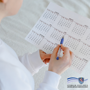 Eine Person in weißem Pullover hält einen ausgedruckten Jahreskalender in der Hand. Mit einem Kugelschreiber markiert sie ein Datum im Juni. Das Motiv deutet auf die Planung oder Nachverfolgung eines persönlichen Zyklus hin. Im unteren rechten Bildbereich befindet sich das Logo des Schwalm-Eder-Kreises mit dem Schriftzug: „Der Kreis mit den schönsten Ecken“.