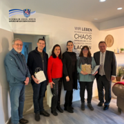 Gruppenfoto in einem Innenraum mit sechs Personen, die nebeneinander stehen. Eine Person hält eine Urkunde und ein Präsent in den Händen. An der Wand im Hintergrund steht ein dekorativer Schriftzug. Von links: DTV-Prüfer Dieter Trinks, Bürgermeister Achim Siebert, Tatjana Grau-Becker (Fachbereichsleiterin Wirtschaftsförderung Schwalm-Eder-Kreis), Kurdirektorin Natascha Rath, Gastgeberin Silke Müller und Landrat Winfried Becker. Oben links ist das Logo des Schwalm-Eder-Kreises zu sehen.