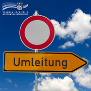 Zwei Verkehrsschilder vor blauem Himmel mit weißen Wolken: oben ein rotes Verbotsschild („Einfahrt verboten“), darunter ein gelbes Hinweisschild mit schwarzer Aufschrift „Umleitung“ und Pfeil nach rechts. Oben links ist das Logo des Schwalm-Eder-Kreises mit dem Schriftzug „Der Kreis mit den schönsten Ecken“ eingeblendet.