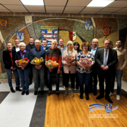 Ein Gruppenfoto zeigt mehrere Frauen und Männer in einem Flur vor einer großen Wandgestaltung mit Wappen und dem Schriftzug „Schwalm-Eder-Kreis“. In der vorderen Reihe halten vier Personen bunte Blumensträuße, rechts steht ein Mann im Anzug. Unten rechts ist das Logo des Schwalm-Eder-Kreises eingeblendet.