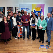 Auf dem Foto steht eine Gruppe von etwa dreizehn Personen in einem hellen Raum vor einer Wand mit farbenfrohen Gemälden und Bannern des Schwalm-Eder-Kreises. Drei Personen in der Mitte halten Trophäen in den Händen. Alle lächeln in die Kamera, und es herrscht eine feierliche, freundliche Stimmung. Im Vordergrund ist der Holzboden zu sehen, im Hintergrund das Logo des Schwalm-Eder-Kreises mit dem Schriftzug „Der Kreis mit den schönsten Ecken“.