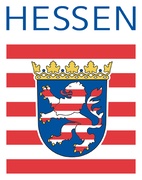 Logo des Bundeslandes Hessen. Oben steht in blauen Großbuchstaben: „HESSEN“. Darunter befindet sich das hessische Landeswappen: Ein rot-weiß gestreifter, goldgekrönter Löwe auf blauem Schild, umgeben von einer stilisierten rot-weißen Fahne mit horizontalen Streifen. Das Wappen ist von einer goldenen Laubkrone gekrönt.