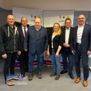 Sechs Erwachsene stehen nebeneinander in einem Innenraum und blicken in die Kamera. Sie tragen überwiegend dunkle Alltags- oder Businesskleidung. Hinter ihnen sind zwei Roll-up-Banner mit der Aufschrift „Kleine Riesen“ zu sehen. Unten links im Bild befindet sich das Logo des Schwalm-Eder-Kreises.