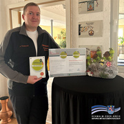 Nils Kreidewolf, Inhaber des Restaurants und der Pension Bürgerhof in Bad Zwesten, steht in einem Gastraum und hält eine Plakette mit der Aufschrift „Wanderbares Deutschland – Qualitätsgastgeber“ in der Hand. Auf einem schwarzen Stehtisch vor ihm liegen die zugehörige Urkunde und eine dekorative „Willkommen“-Steinfigur mit kleinen Schildkröten. Unten rechts ist das Logo des Schwalm-Eder-Kreises mit dem Schriftzug „Der Kreis mit den schönsten Ecken“ eingeblendet.