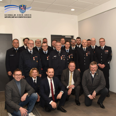 Gruppenbild mit rund 20 Personen bei einer Ehrungsveranstaltung. Die meisten Personen tragen Feuerwehr-Uniformen, mehrere von ihnen sind mit goldenen Brandschutzehrenzeichen ausgezeichnet. In der vorderen Reihe knien fünf Personen: Marcel Pritsch (Bürgermeister Borken), Kreisbrandinspektorin Tanja Dittmar, Luca Fritsch (Bürgermeister Willingshausen), Landrat Winfried Becker und Frank Grunewald (Bürgermeister Niedenstein). Im Hintergrund stehen die weiteren Geehrten und Beteiligten in mehreren Reihen. Links oben ist das Logo des Schwalm-Eder-Kreises mit dem Schriftzug „Der Kreis mit den schönsten Ecken“ zu sehen.