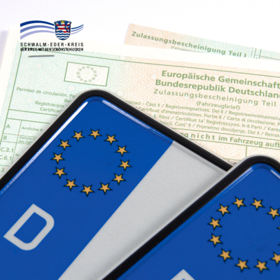 Auf dem Bild sind zwei Kfz-Kennzeichen mit blauem EU-Feld und dem Buchstaben „D“ für Deutschland zu sehen. Im Hintergrund liegt eine Zulassungsbescheinigung Teil I der Bundesrepublik Deutschland. Oben links ist das Logo des Schwalm-Eder-Kreises eingeblendet.