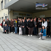 Eine größere Gruppe von Jugendlichen und Erwachsenen steht vor dem Eingang eines öffentlichen Gebäudes unter einem überdachten Bereich. Einige Personen stehen, andere hocken vorne, alle blicken in die Kamera. Über dem Eingang sind Hinweisschilder angebracht, rechts oben im Bild ist das Logo des Schwalm-Eder-Kreises zu sehen.