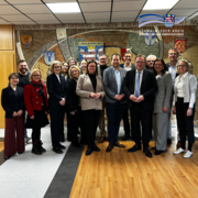 Mehrere Erwachsene stehen in einem Innenraum nebeneinander und blicken in die Kamera. Sie tragen überwiegend Business- oder gepflegte Alltagskleidung. Im Hintergrund ist eine große Wandgestaltung mit dem Schriftzug „Schwalm-Eder-Kreis“ sowie Wappen verschiedener Städte und Gemeinden zu sehen. Oben rechts ist zusätzlich das Logo des Schwalm-Eder-Kreises eingeblendet.